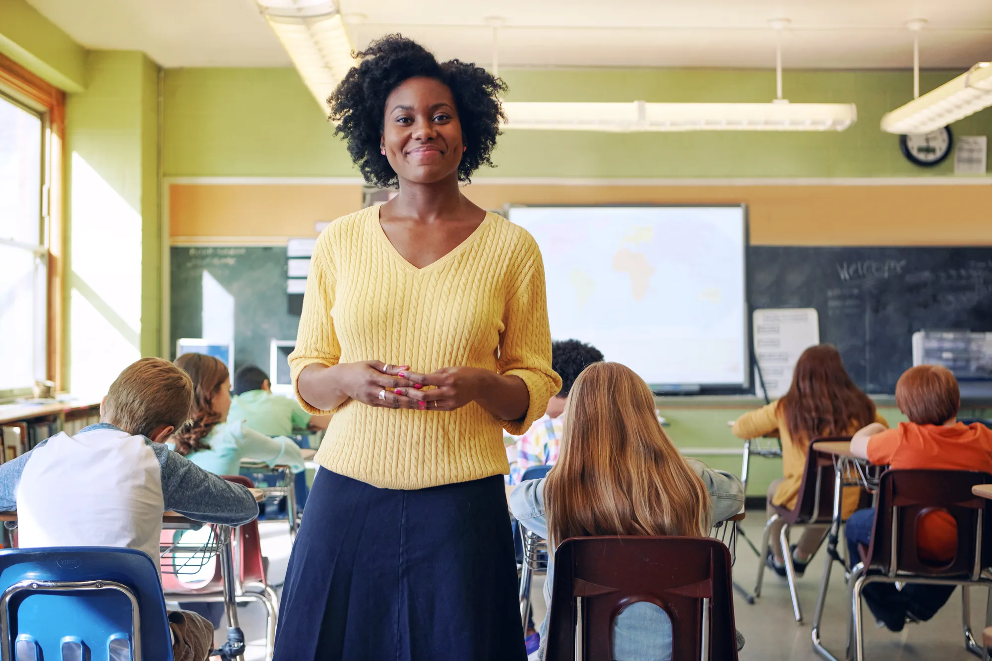 A New Jersey teacher, standing in her class smiling at the camera.