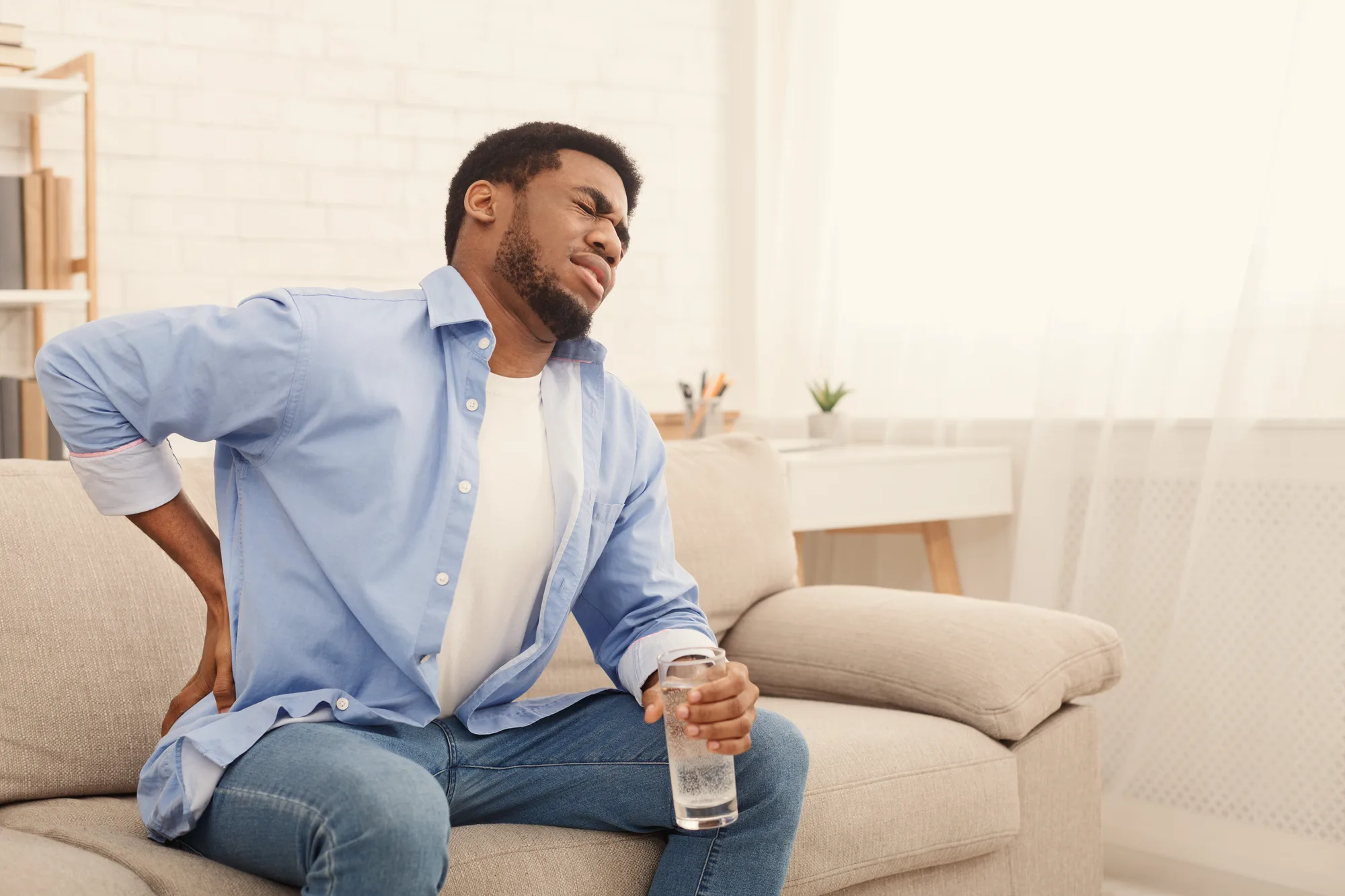 Young black man in New Jersey experiencing lower back pain while sitting on a couch.