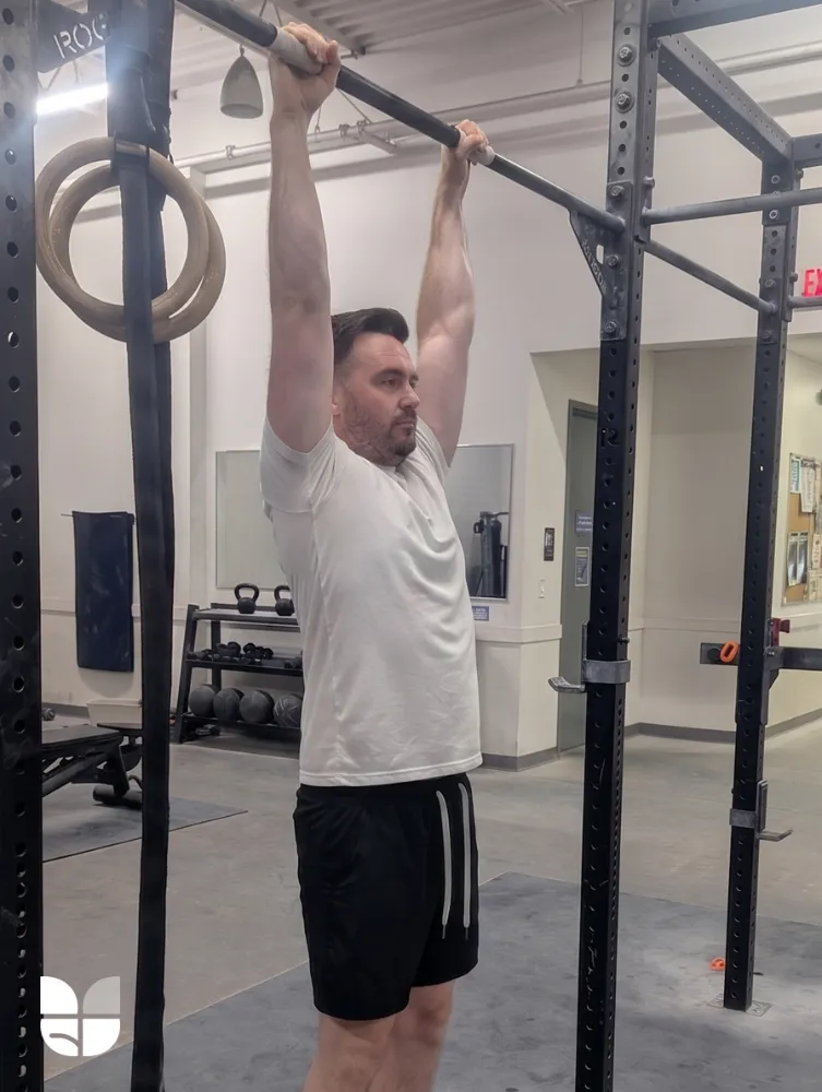 Man doing a leg raise exercise for spinal health, hanging from a bar with his hands, and relaxing his core.